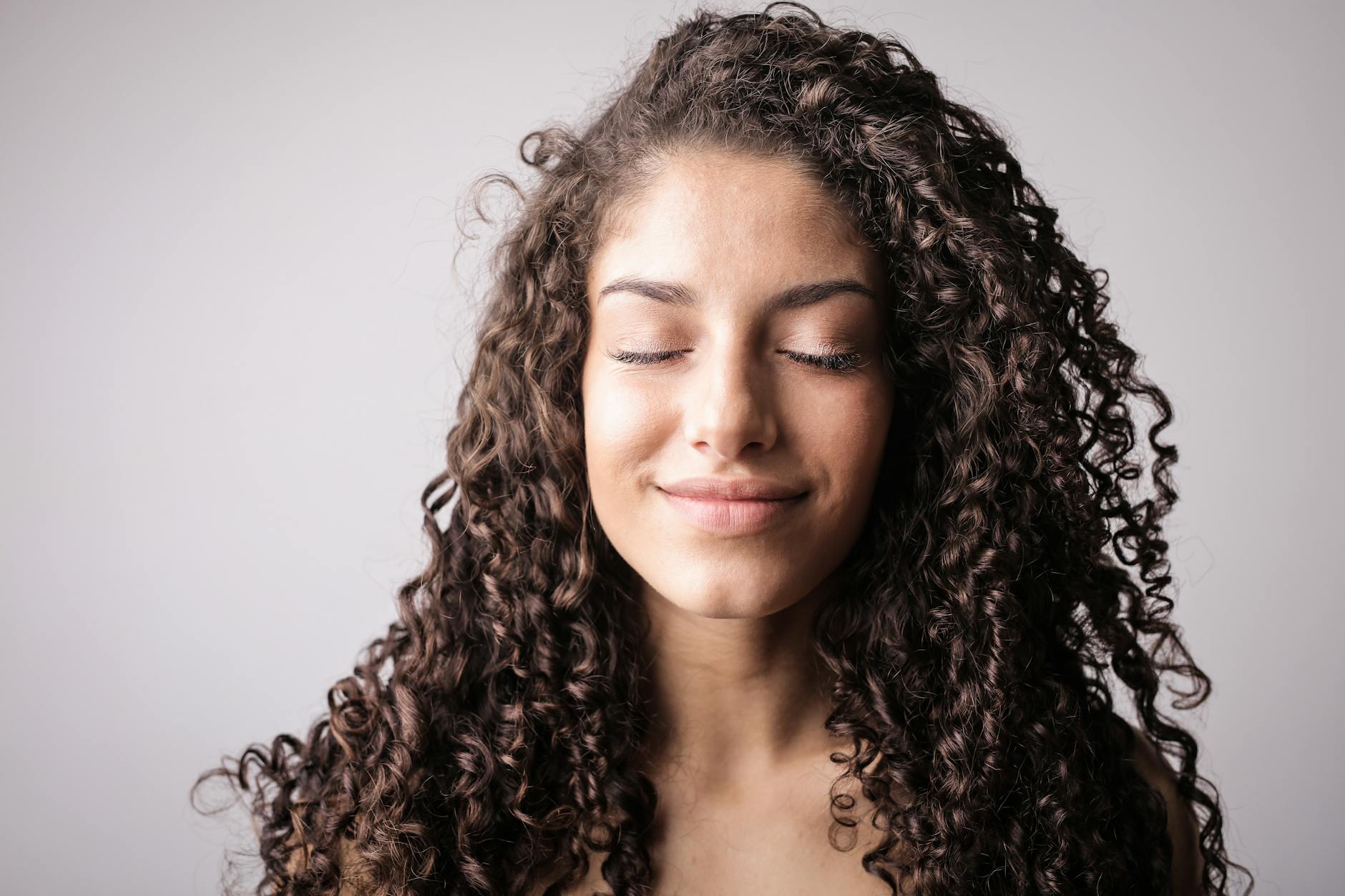 portrait photo of smiling woman with brown curly hair with her eyes closed